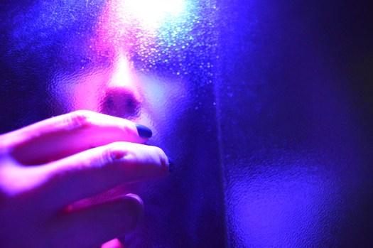 Marcela's face behind a glass wall, with her hand covering her mouth in front of the wall.